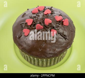 Schoko-Muffin mit roten Zuckerherzen auf einem Teller grün Stockfoto