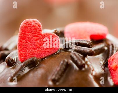 Detail von einem Schoko-Muffin mit roten Zuckerherzen und Streuseln Stockfoto