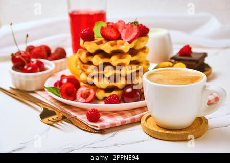 Belgische Waffeln mit Erdbeeren, Aprikosen, Kirschen, Saft und einer Tasse schwarzen Kaffees Stockfoto