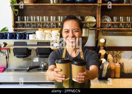 Vietnamesische lächelnde Kellnerin hielt Pappbecher mit Kaffee in einem Café Stockfoto