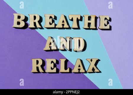 Atmen und entspannen Sie sich, Wörter in hölzernen Buchstaben isoliert auf violettem Hintergrund Stockfoto