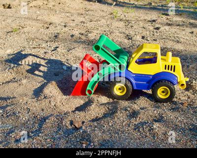 Plastik-Spielzeugwagen mit Schatten im Sandkasten auf dem Kinderspielplatz im Sommer im Freien. Stockfoto