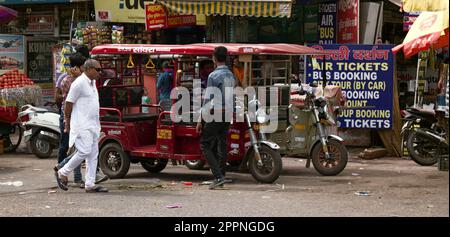 Indien, Neu-Delhi - 1. März 2018: Markt- und elektrische Rikscha-Taxis auf der Straße. Landschaft einer gewöhnlichen indischen Stadt. Stockfoto