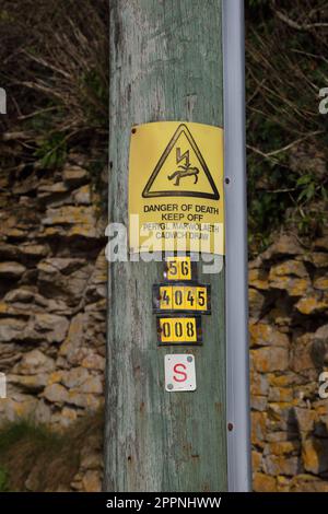 Ein Hochstrompolster steht in einem ländlichen Raum mit einem Warnschild in englischer und walisischer Sprache, das auf die Gefahr hinweist. Stockfoto