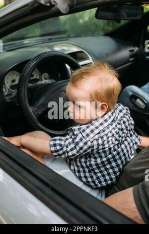 Papa zeigt seinem kleinen Sohn, wie er das Auto fährt, während er hinter dem Steuer sitzt Stockfoto