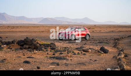 Rotes Auto parkt in einer flachen Wüstenlandschaft in der Nähe von Piedra playa („Stone Beach“) im Norden von Fuerteventura auf den Kanarischen Inseln, Spanien Stockfoto