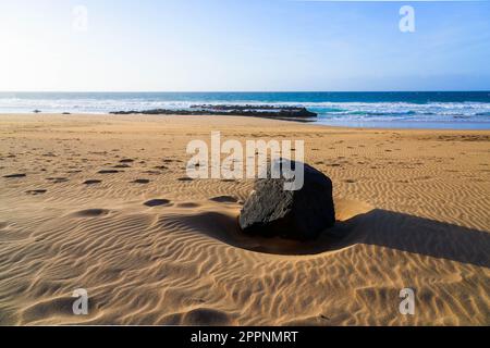 Einsamer Felsbrocken auf dem gewellten Sand von Playa de la Escalera (Treppenstrand) an der Westküste von Fuerteventura auf den Kanarischen Inseln, Atlant Stockfoto