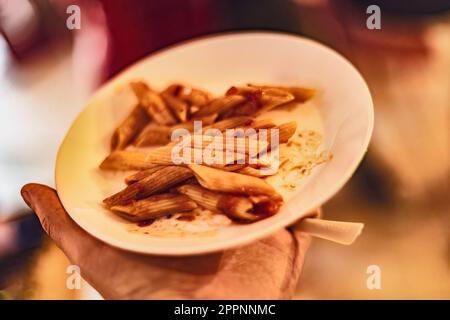 Nahaufnahme einer Hand mit einem Teller köstlicher Pasta, die Sie genießen können. Stockfoto