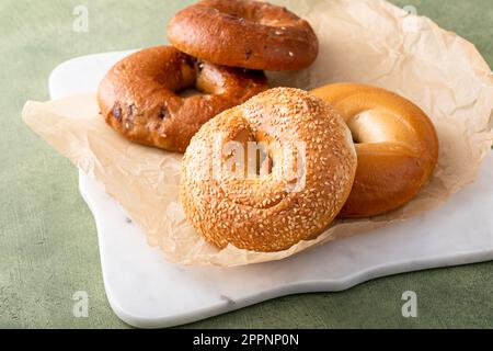 Hausgemachte, frisch gebackene Bagels auf Pergamentpapier, verzehrfertig, Zimtrosinen, Sesam und Bagel Stockfoto