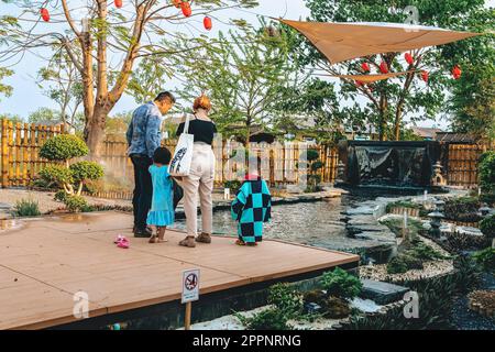 KANCHANABURI -THAILAND, 30. MÄRZ 2023 : Unbekannte Touristen kommen zu Besuch und füttern Koi oder schicke Karpfen in einem kleinen Teich mit schönem Garten Stockfoto