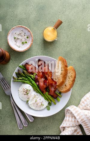 Gesundes Frühstück mit pochierten Eiern, Speck und Spargel serviert mit Hollandaise-Sauce Stockfoto