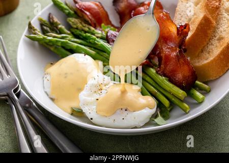 Gesundes Frühstück mit pochierten Eiern, Speck und Spargel serviert mit Hollandaise-Sauce Stockfoto
