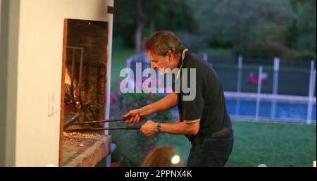 Ein aufrichtiger älterer Mann, der Barbecue zubereitet. Zwanglose leitende Person, die Feuermehl zubereitet Stockfoto