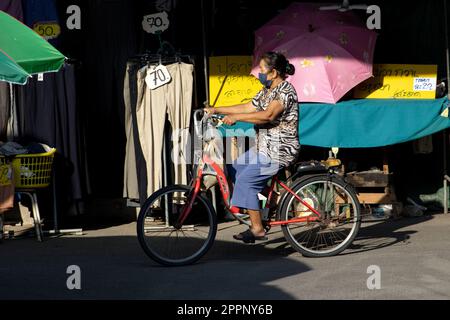 SAMUT PRAKAN, THAILAND, FEBRUAR 07 2023, Eine Frau fährt auf einem Fahrrad auf dem Marktplatz neben einem Stand Stockfoto