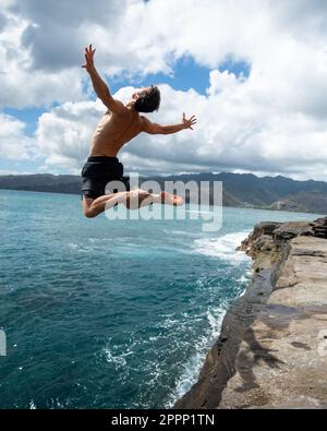 Ein Mann, der von der Spitting Cave auf Oahu, Hawaii, springt. Hochwertiges Foto Stockfoto