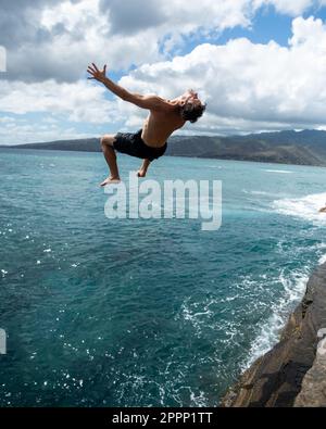 Ein Mann, der von der Spitting Cave auf Oahu, Hawaii, springt. Hochwertiges Foto Stockfoto