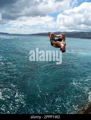 Ein Mann, der von der Spitting Cave auf Oahu, Hawaii, springt. Hochwertiges Foto Stockfoto