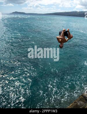 Ein Mann, der von der Spitting Cave auf Oahu, Hawaii, springt. Hochwertiges Foto Stockfoto