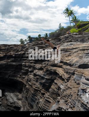 Ein Mann, der von der Spitting Cave auf Oahu, Hawaii, springt. Hochwertiges Foto Stockfoto