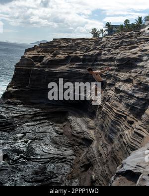 Ein Mann, der von der Spitting Cave auf Oahu, Hawaii, springt. Hochwertiges Foto Stockfoto