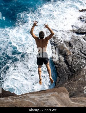 Ein Mann, der von der Spitting Cave auf Oahu, Hawaii, springt. Hochwertiges Foto Stockfoto