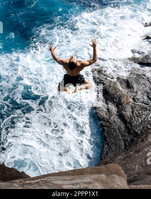 Ein Mann, der von der Spitting Cave auf Oahu, Hawaii, springt. Hochwertiges Foto Stockfoto