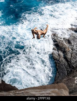 Ein Mann, der von der Spitting Cave auf Oahu, Hawaii, springt. Hochwertiges Foto Stockfoto