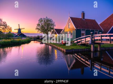 In der Dämmerung bietet sich ein spektakulärer Blick auf das traditionelle holländische Dorf Zaanse Schans mit seinen Windmühlen, die sich im Wasser des Kanals spiegeln, und den Häusern illumi Stockfoto