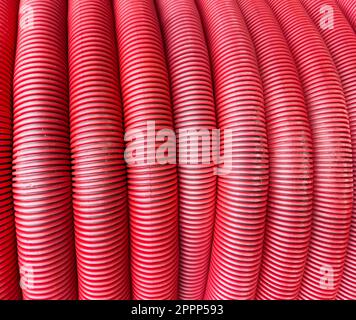 HDPE-Wellrohrstruktur Hintergrund. Schutz für unterirdische Kabel. Aufgerolltes rotes gewelltes PVC-Rohr. Rote Baurohre. Beschichtete Wellkonstruktion Stockfoto