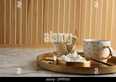 Raffinierte Zuckerwürfel in der Schüssel und aromatischer Tee auf einem weißen Marmortisch. Platz für Text Stockfoto