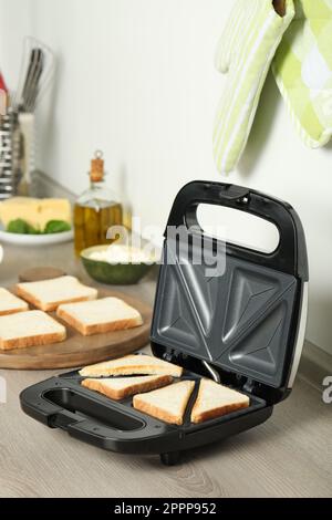 Moderner Sandwichmaker mit Brotscheiben auf Holztisch Stockfoto