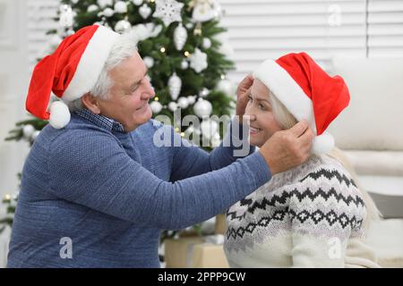 Glückliches, reifes Paar in Weihnachtsmannhüten zu Hause. Weihnachtsfeier Stockfoto