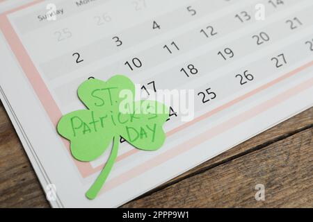 Papier Kleeblatt mit den Worten ST. PATRICKS TAG und Kalender auf Holzhintergrund Stockfoto