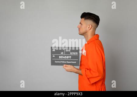Verbrecherfoto eines Gefangenen in orangefarbener Uniform mit Brett auf grauem Hintergrund, Seitenansicht Stockfoto