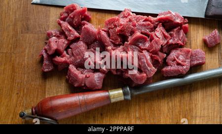 Herefordshire gewürfeltes Rindfleisch auf einem Holztisch mit einem rustikalen Messer und Stahl. Stockfoto