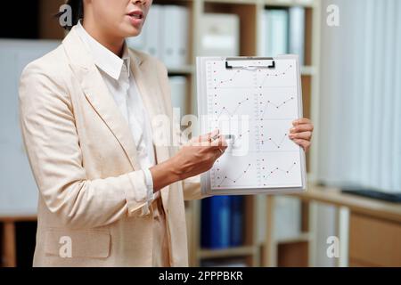 Zugeschnittene Aufnahme einer jungen Analystin- oder Maklerin, die grafische Daten meldet, während sie auf ein Dokument in der Zwischenablage des Geschäftsseminars zeigt Stockfoto