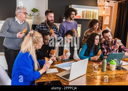 Arbeitsgruppe führt während einer Pause eine Diskussion über den Verzehr von Croissants. Imbiss am Arbeitsplatz zur Verbesserung der Effizienz Stockfoto