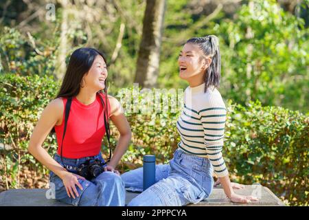 Glückliche asiatische Frauen, die sich während einer Wanderung im Wald ausruhen Stockfoto