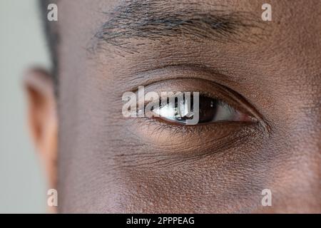 Nahaufnahme des Gesichts eines Afrikaners. Augenmakro mit schwarzer Iris. Nahaufnahmen und sichtbare männliche Merkmale. Wimpern und Augenbrauen in Ordnung. Stockfoto