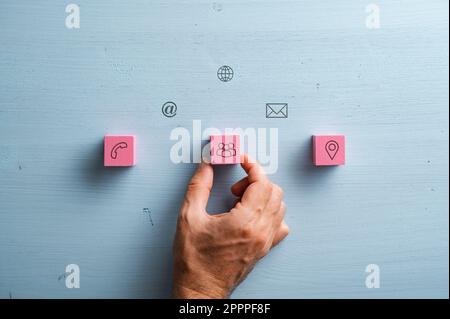 Kontakt- und Kommunikationssymbole und -Symbole sind auf pinkfarbenen Holzblöcken und hellblauem Holzhintergrund aufgedruckt. Stockfoto