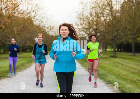Reife Dame führt eine Gruppe von Läuferinnen, die in der Natur trainieren. Der Begriff der körperlichen Leistungsfähigkeit auch im Alter. Stockfoto