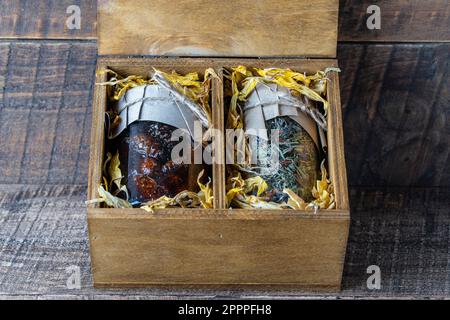 Glasbecher mit Blumentee und Glasbecher mit Kiefernkonfitüre in einer hölzernen Geschenkbox auf einem Tisch, Nahaufnahme. Schönes Geschenk für Familie und Freunde Stockfoto