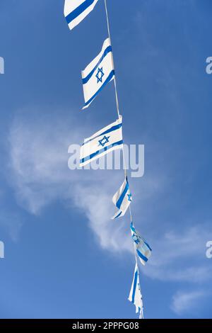 Blaues und weißes Fähnchen, das vor dem Hintergrund des blauen Himmels mit weißen Wolken am Unabhängigkeitstag Israels flattert. Perfekt für Projekte im Zusammenhang mit israelischer Kultur und Feiern. Stockfoto