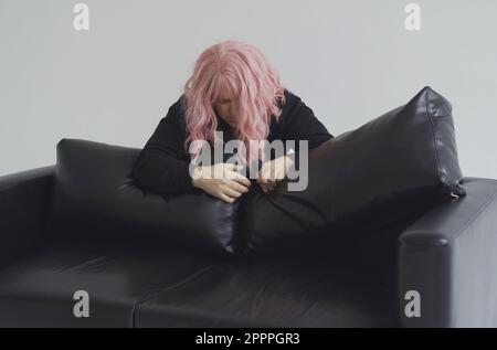 Ein betrunkener Mann in einer rosa Perücke klettert über das Sofa und schläft ein. Stockfoto