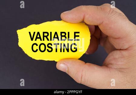 Geschäftskonzept. Auf schwarzem Hintergrund, in den Händen eines Mannes, ein gelber zerrissener Karton mit der Aufschrift "Variable Costing" Stockfoto