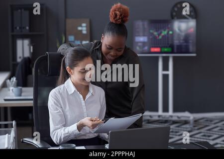 Junge Kollegen analysieren Finanzdokumente zusammen, während sie am Tisch im Maklerbüro sitzen Stockfoto