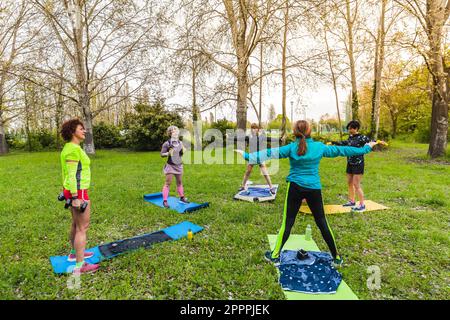 Eine Gruppe von Damen, die im Park auf Matten im Gras einer Wiese Gymnastik machen. Fitnesskonzept für alle Altersgruppen. Stockfoto