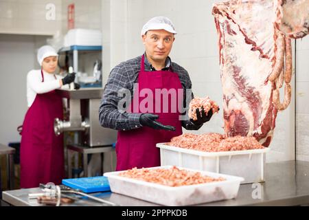 Positiver männlicher Metzger, der Hackfleisch in der Metzgerei macht Stockfoto