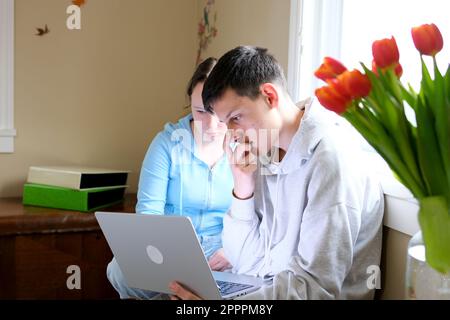 Ein Junge und ein Mädchen sitzen neben einem Computer ein Junge kratzt Pickel mit seinen Händen er bemerkt sich nicht die übliche Umgebung Teenager Ausschläge auf dem Gesicht Pickel auf Kinn und Wange Stockfoto