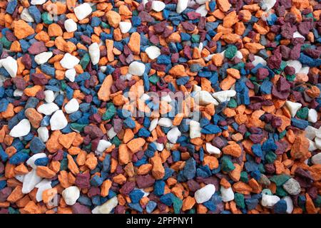 Kleine Kieselsteine in leuchtender Farbe, der Hintergrund ist blau, weiß, orange, burgunderrot. Stockfoto